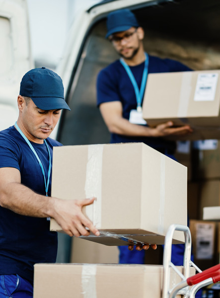 young-courier-his-colleague-unloading-cardboard-boxes-from-delivery-van (1) (1)